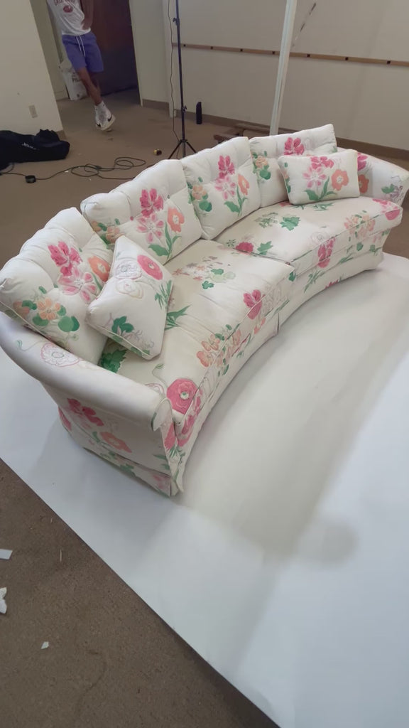 A curved, vintage floral sofa featuring pink flowers on a white background. 