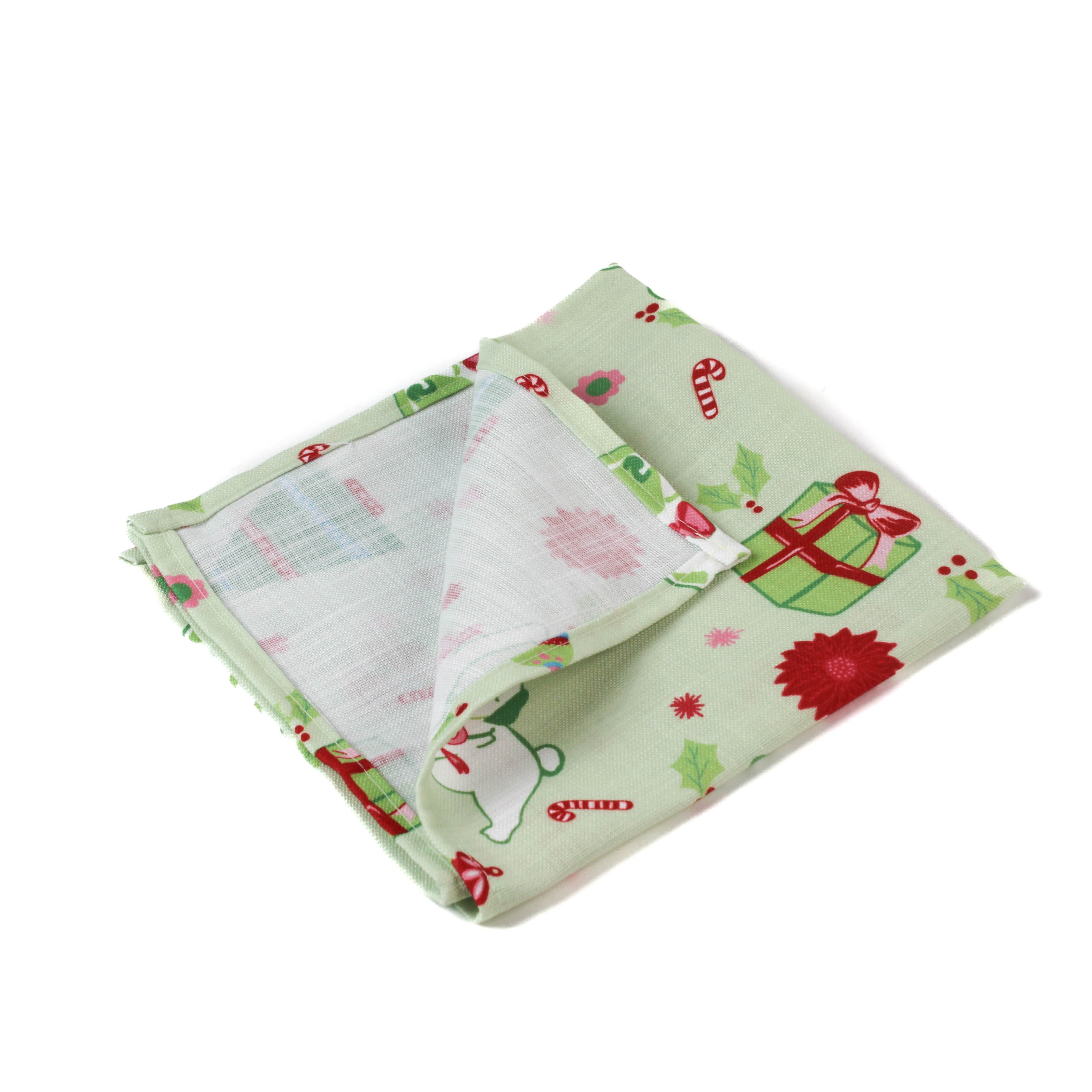 a folded green christmas napkin with pugs, christmas trees and candy cane motift on a white background