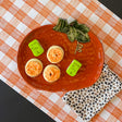 a large orange pumpkin serving platter with 5 halloween cookies on it against an orange paper halloween table runner. 