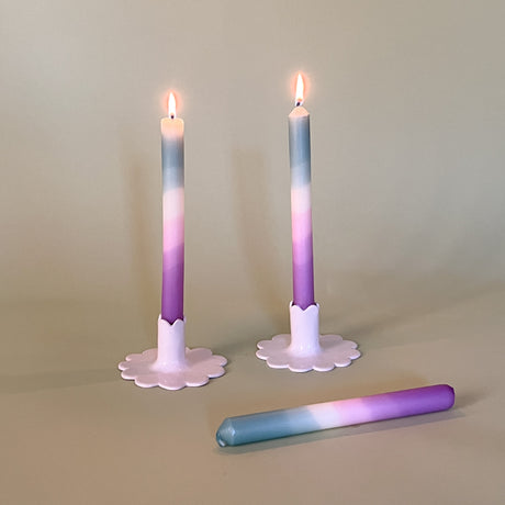 two purple and blue taper candles in white ceramic candle holders