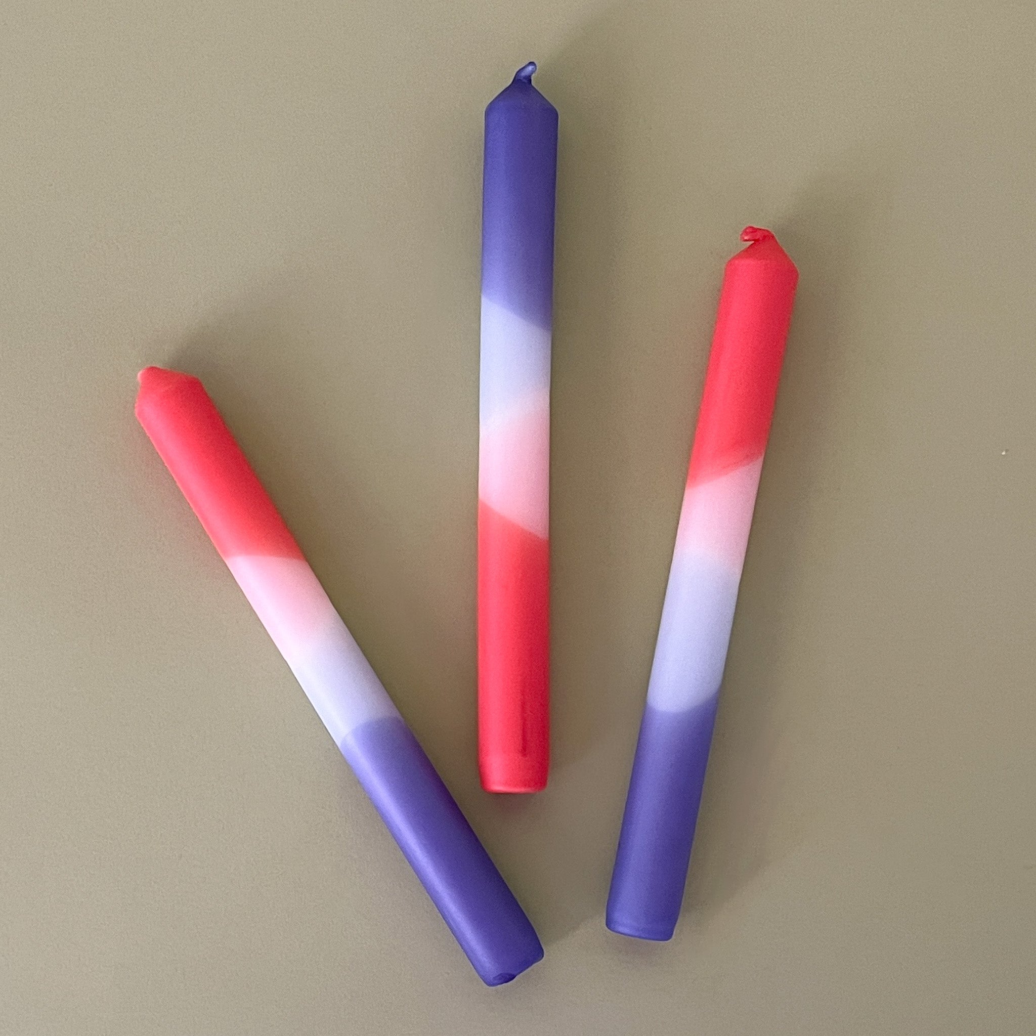 a trio of colorful taper candles in a mix of white, purple and hot pink. 