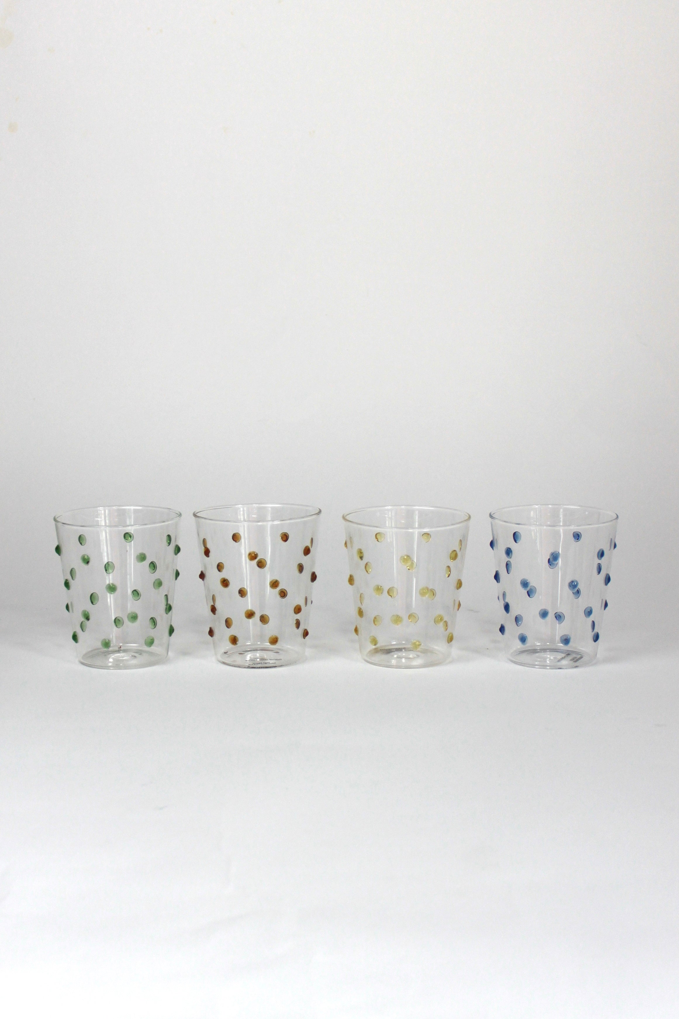 four glasses with raised dot embellishments, one green, one brown, one yellow and one blue