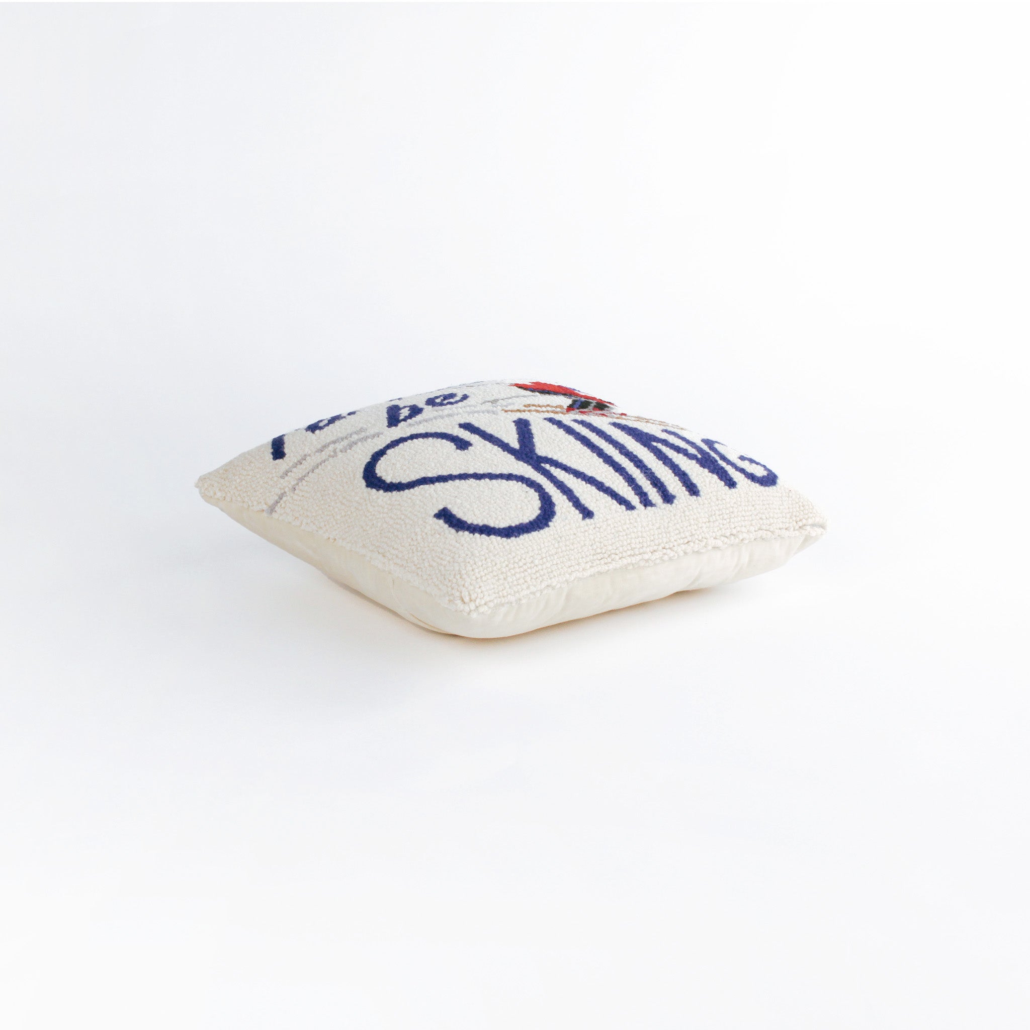 side of a Square decorative pillow with a skier in a red jacket and blue helmet on snowy slopes, featuring the phrase “I’d rather be SKIING” in bold blue text.