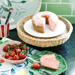a rattan pedestal bowl holding a cake and surround by strawberry decor in a green kitchen. 