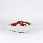side of a Hooked wool Christmas pillow featuring a square white design with a large red Christmas bow wrapped in multicolored holiday string lights.