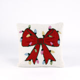 Hooked wool Christmas pillow featuring a square white design with a large red Christmas bow wrapped in multicolored holiday string lights.