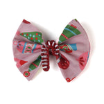 a red candy cane christmas napkin ring filled with a pink christmas napkin with ornament motifs against a white background. 