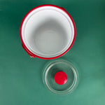 Top view of an open red holiday ice bucket with removable clear lid on a green background