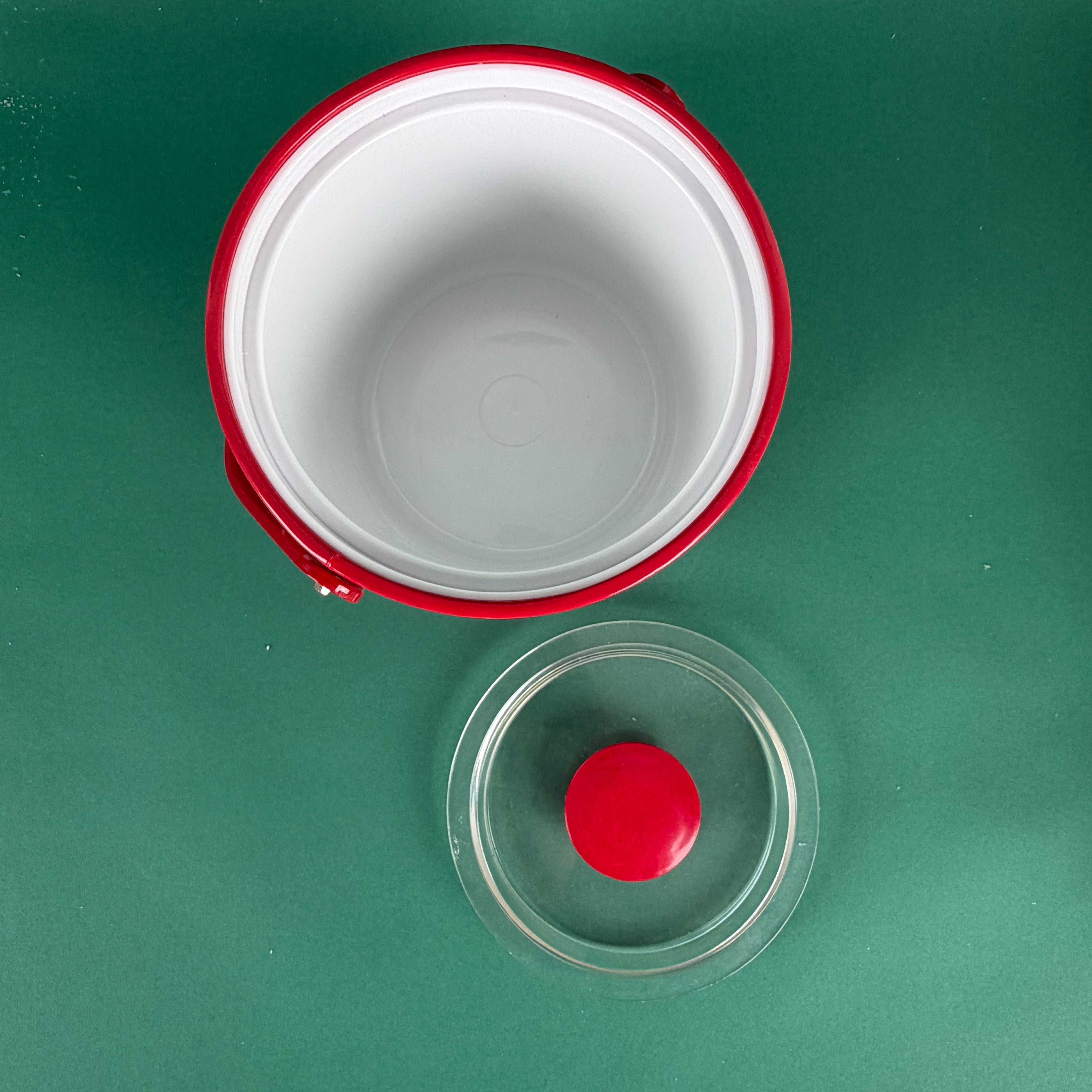 Top view of an open red holiday ice bucket with removable clear lid on a green background
