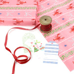 a Pink wrapping paper roll with a festive pattern featuring lobsters, bows, and decorative stripes with red ribbon on wool and assorted gift tags