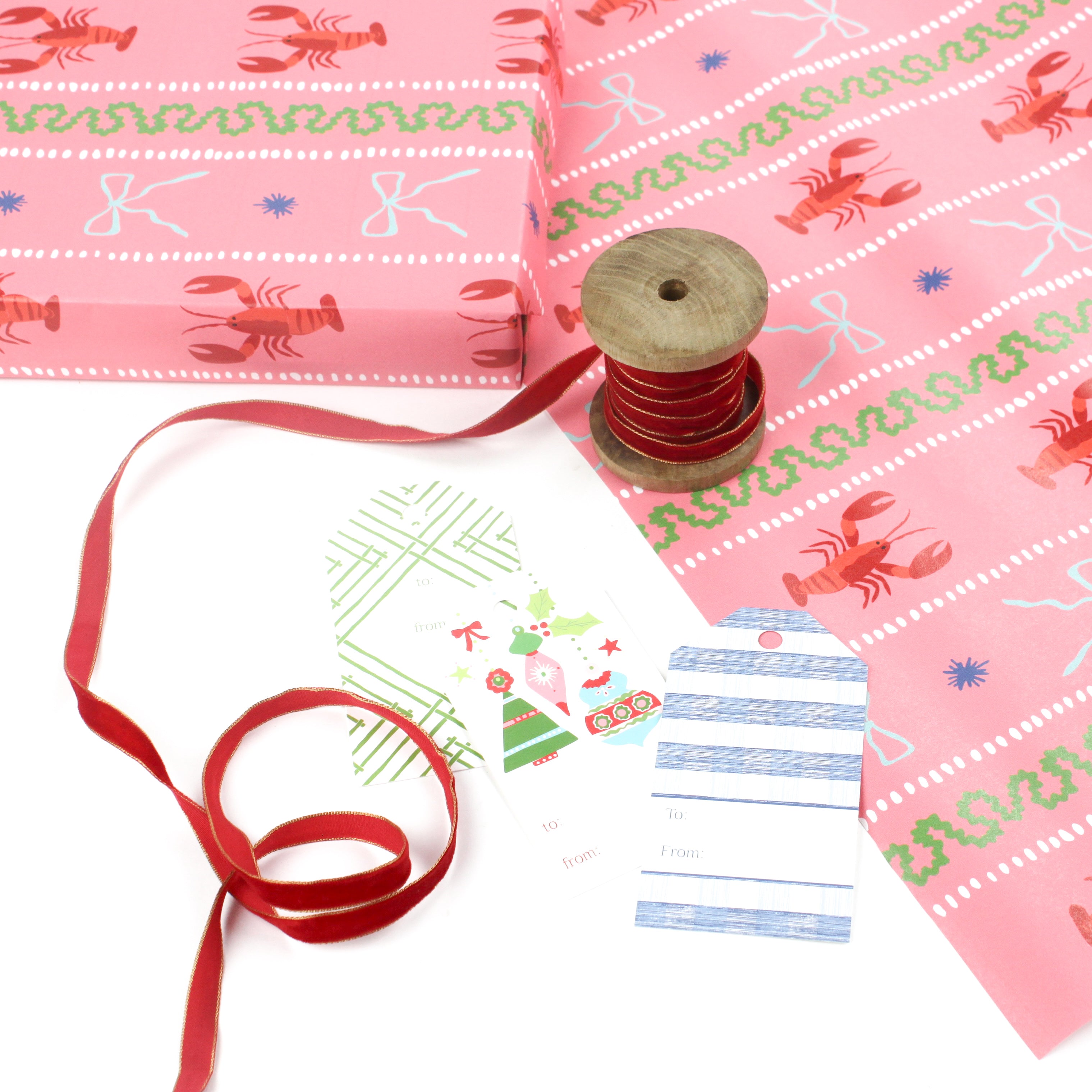 a Pink wrapping paper roll with a festive pattern featuring lobsters, bows, and decorative stripes with red ribbon on wool and assorted gift tags