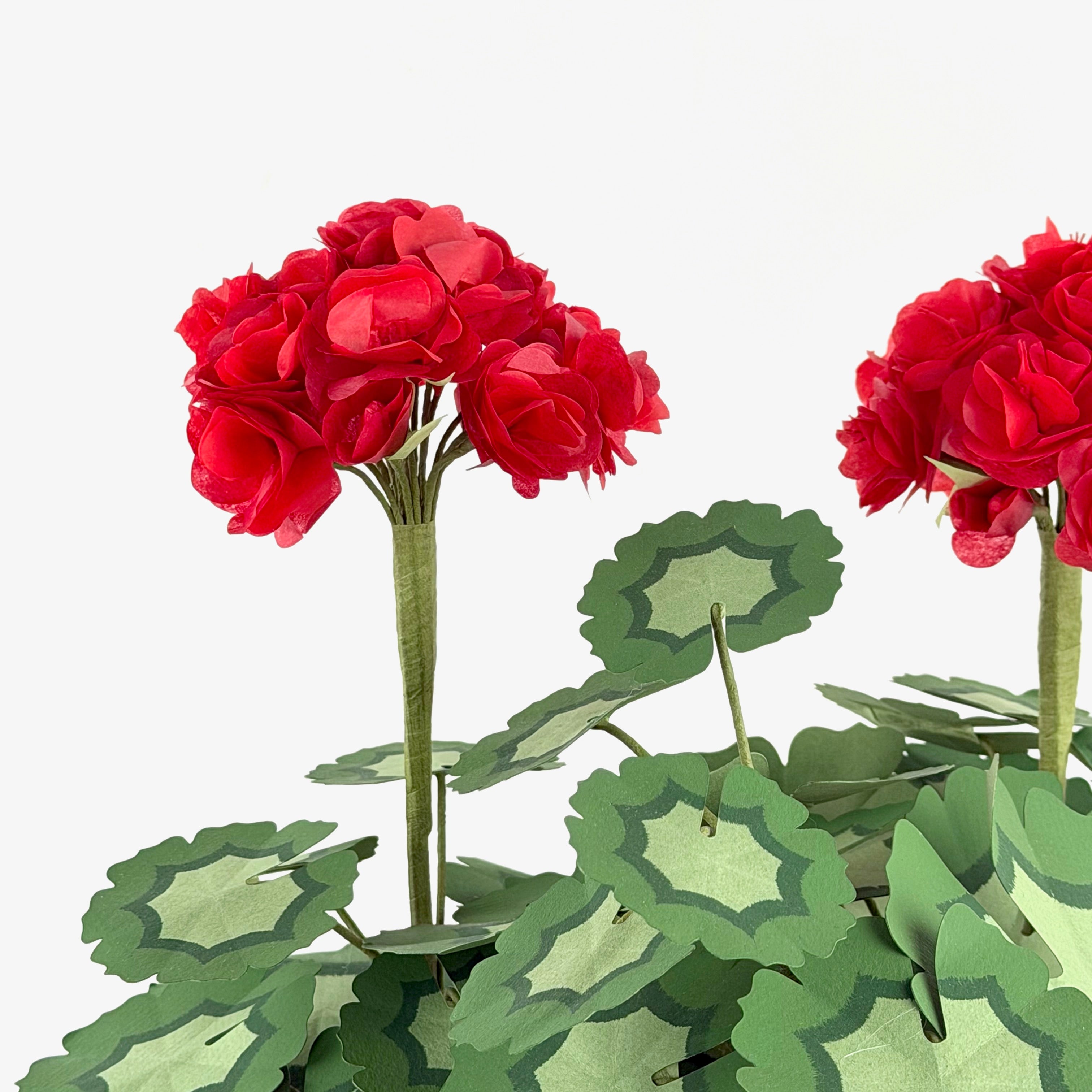 Close-up of a red paper geranium centerpiece featuring layered red blooms and decorative green paper leaves.