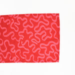 A red christmas table runner with a pink ribbon motif photographed on a white background. 