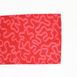 A red christmas table runner with a pink ribbon motif photographed on a white background. 