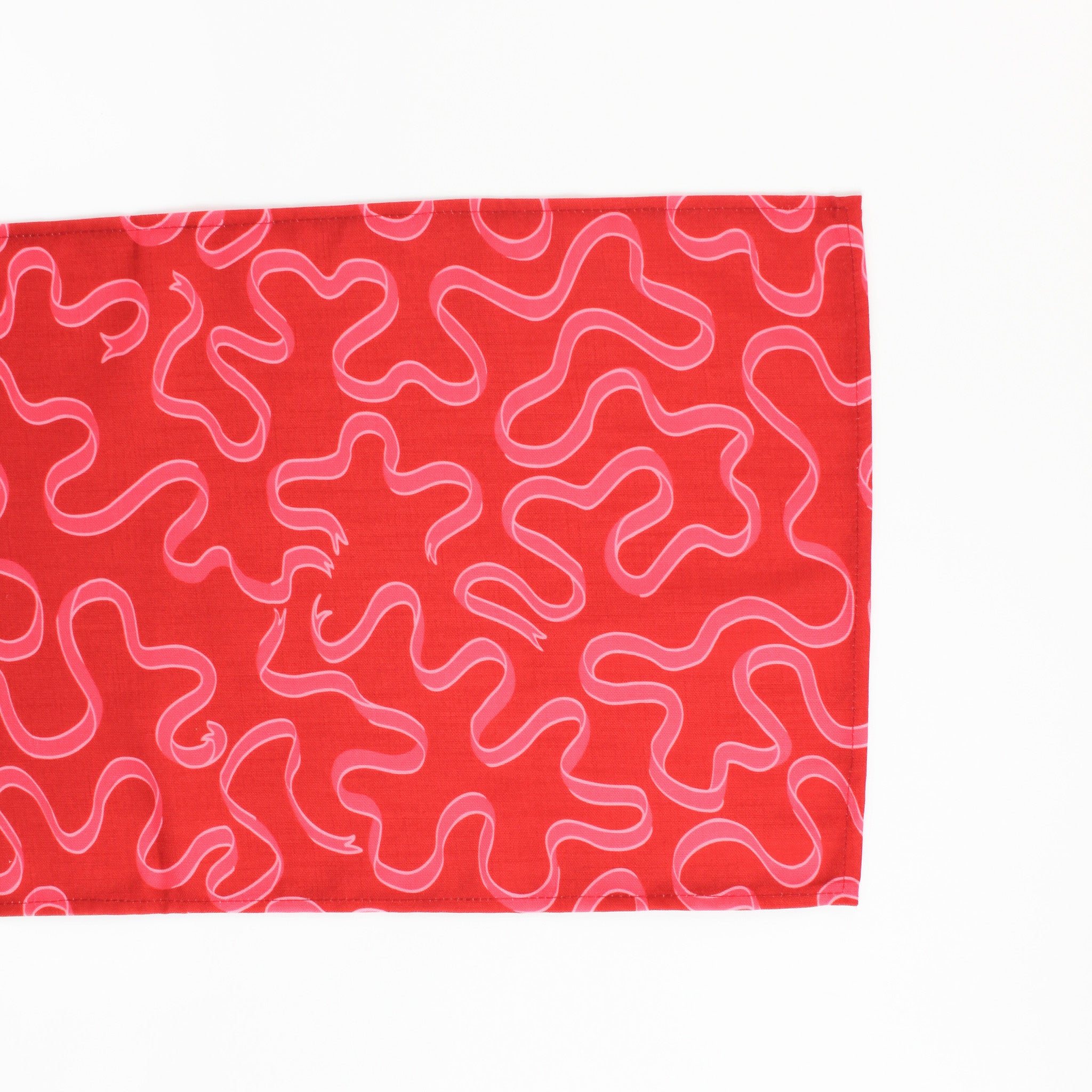 A red christmas table runner with a pink ribbon motif photographed on a white background. 