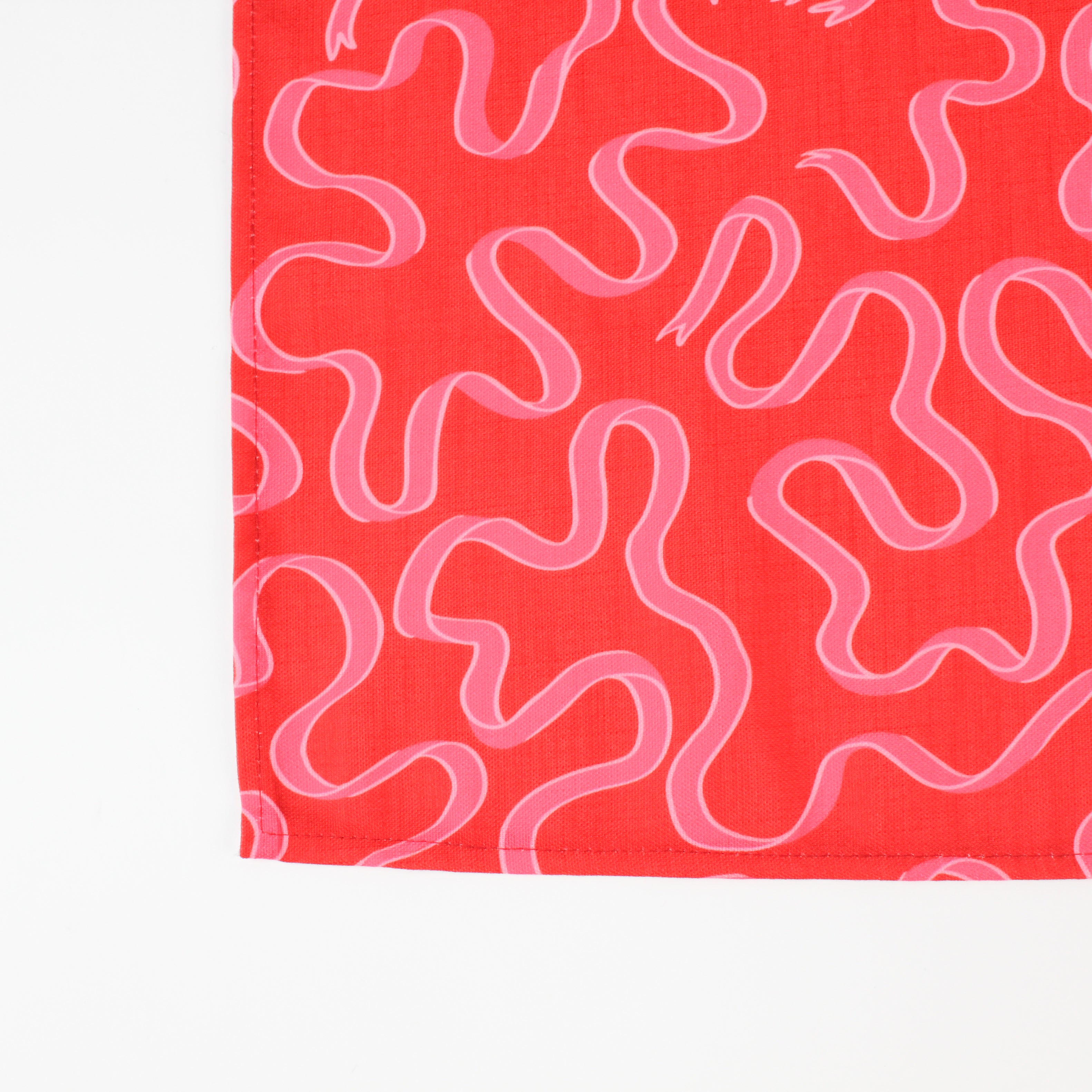 A red christmas table runner with a pink ribbon motif photographed on a white background. 