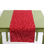 Red table runner with a pink squiggle pattern draped over a light green table.