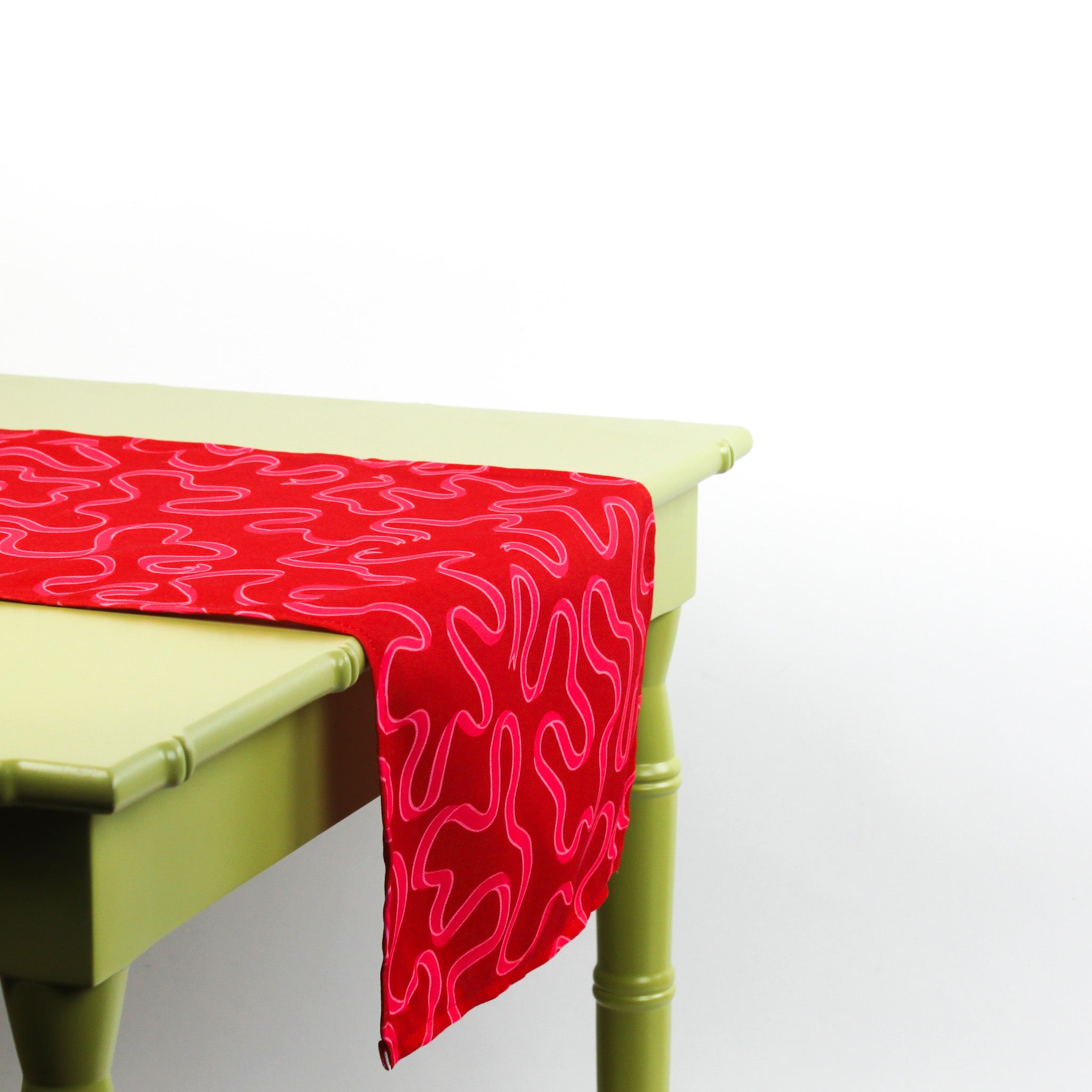 Red squiggle-pattern table runner hanging over the edge of a light green table.