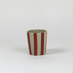A striped ceramic cup in red striped on a white background. 