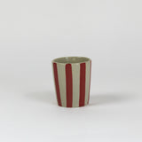 A striped ceramic cup in red striped on a white background. 