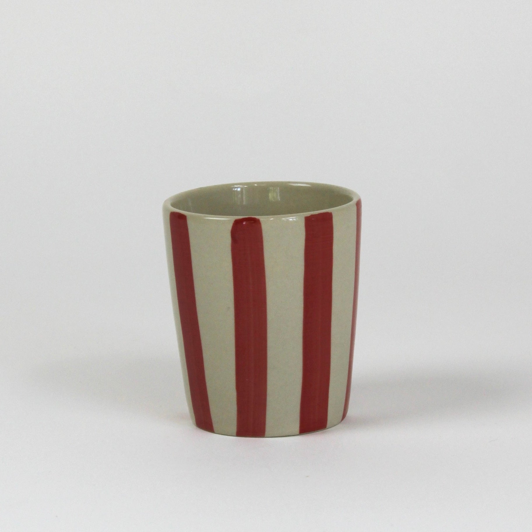 A striped ceramic cup in red striped on a white background. 