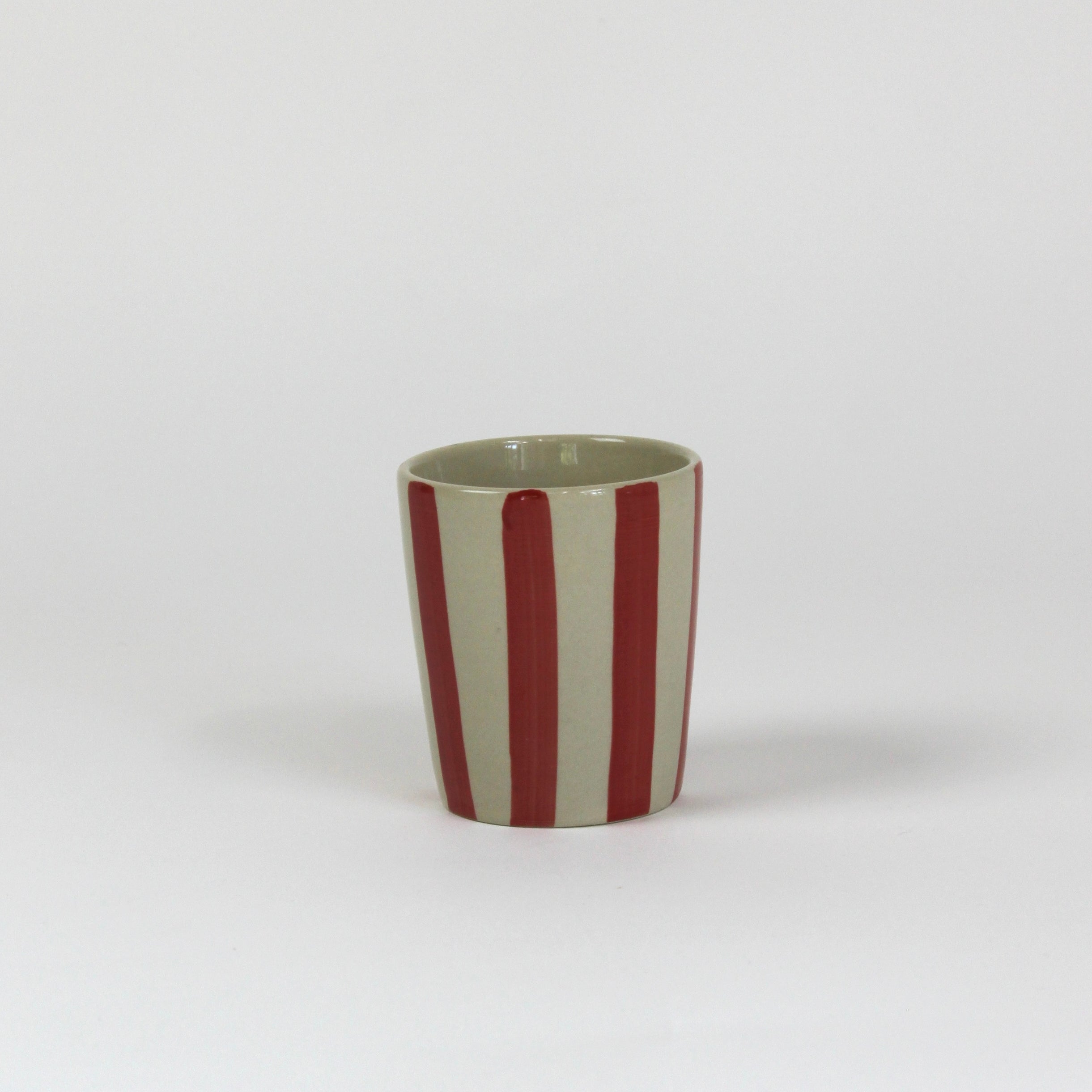 A striped ceramic cup in red striped on a white background. 