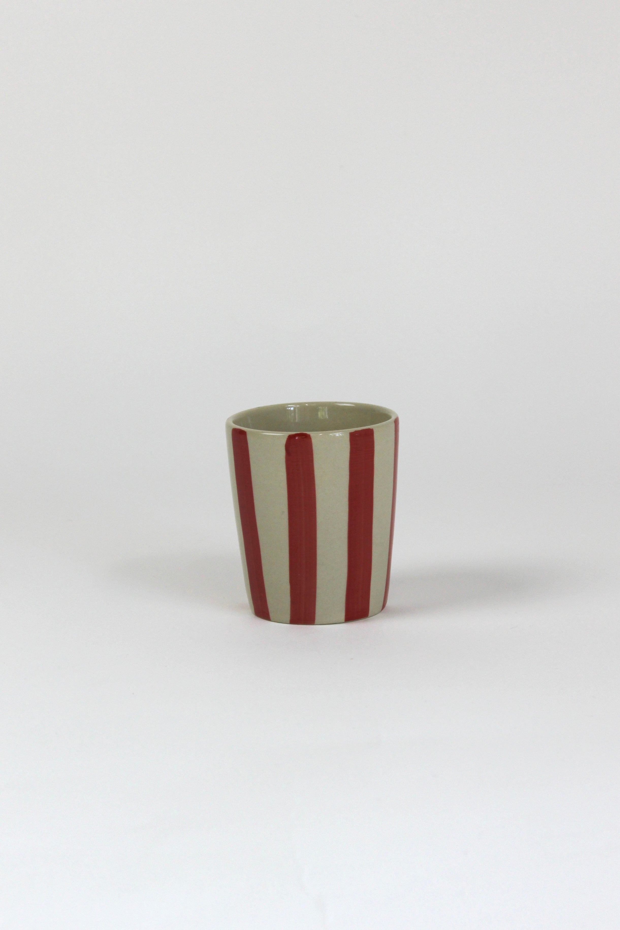 A striped ceramic cup in red striped on a white background. 