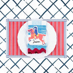 A styled patriotic table setting featuring a red white and blue striped paper placemat, white plate, striped napkin, and decorative place card.