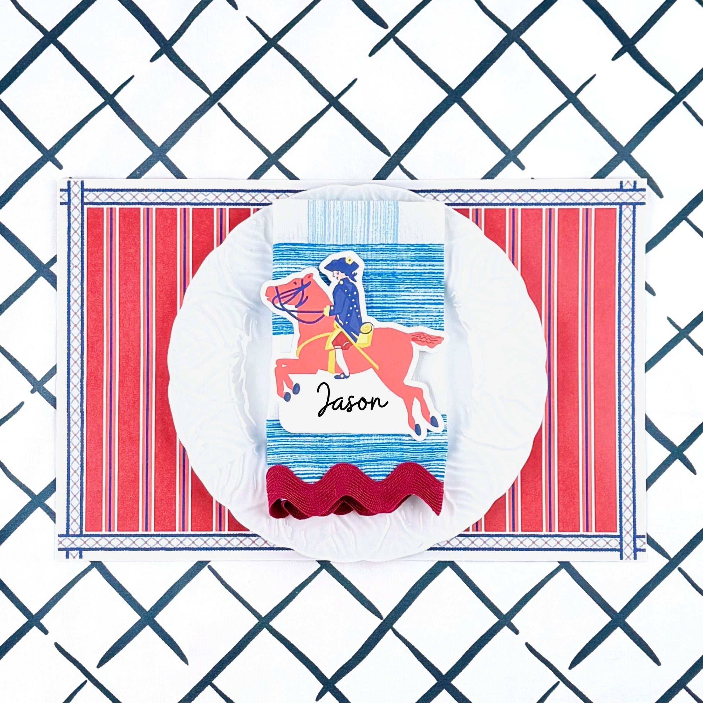 A styled patriotic table setting featuring a red white and blue striped paper placemat, white plate, striped napkin, and decorative place card.
