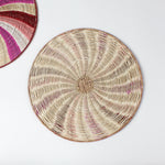 reverse side of a round rattan christmas placemat with pink, red, white and yellow candy-cane like swirls. 