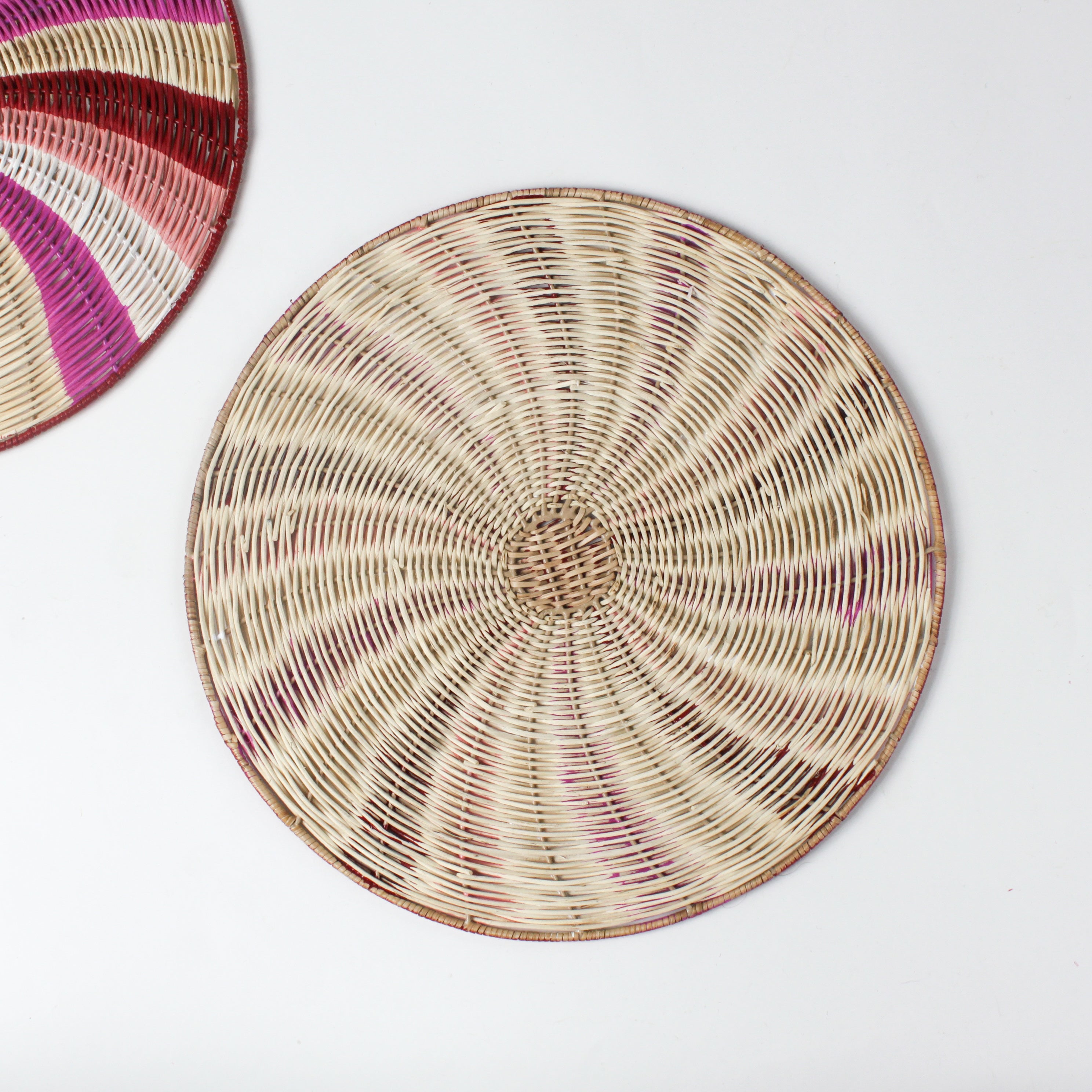 reverse side of a round rattan christmas placemat with pink, red, white and yellow candy-cane like swirls. 