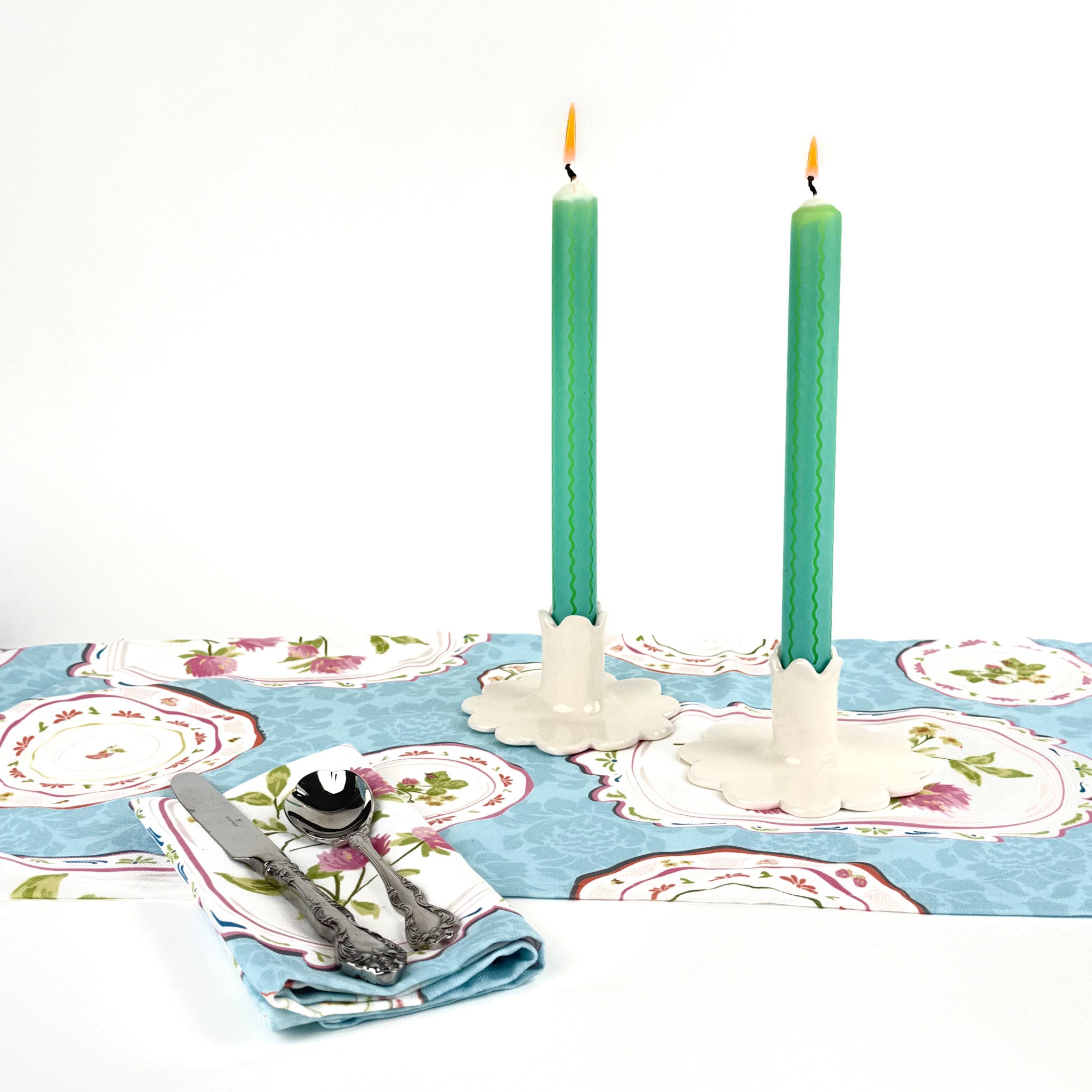 Green and blue ricrac stripe taper candles lit on a spring table setting with floral table linens and candle holders.