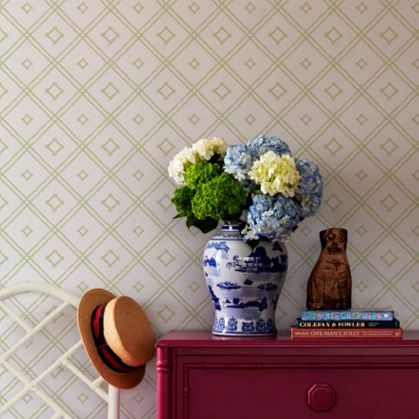 a flower filled vase against a wall of green and white wallpaper in a bamboo trellis design.