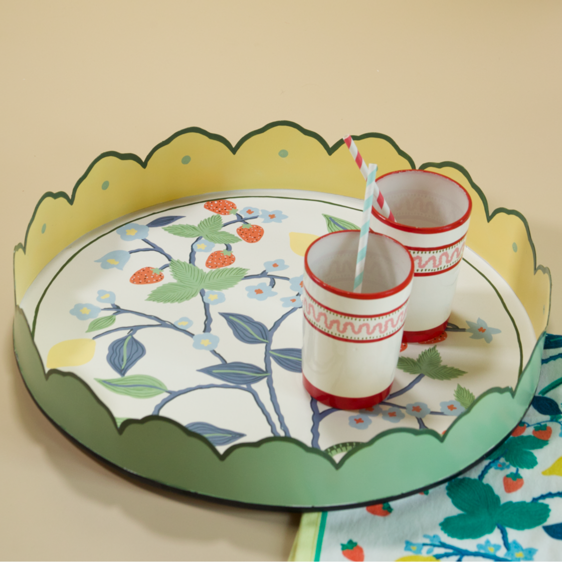 A round tole tray designed by Madcap Cottage with scalloped edges and a handpainted strawberry, blue flower and lemon motifs on the base