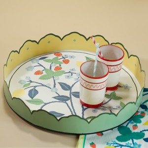 A round tole tray designed by Madcap Cottage with scalloped edges and a handpainted strawberry, blue flower and lemon motifs on the base