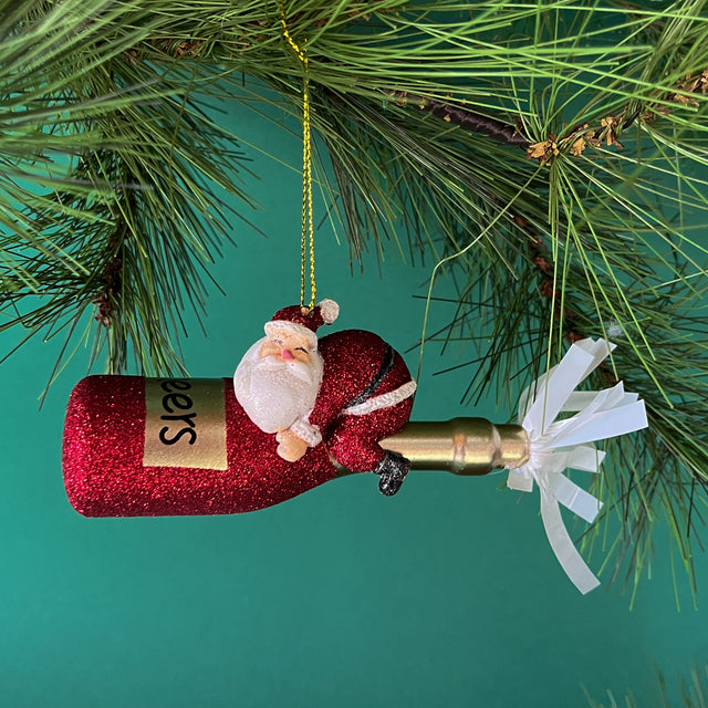 a santa riding a red champagne bottle ornament against a green background