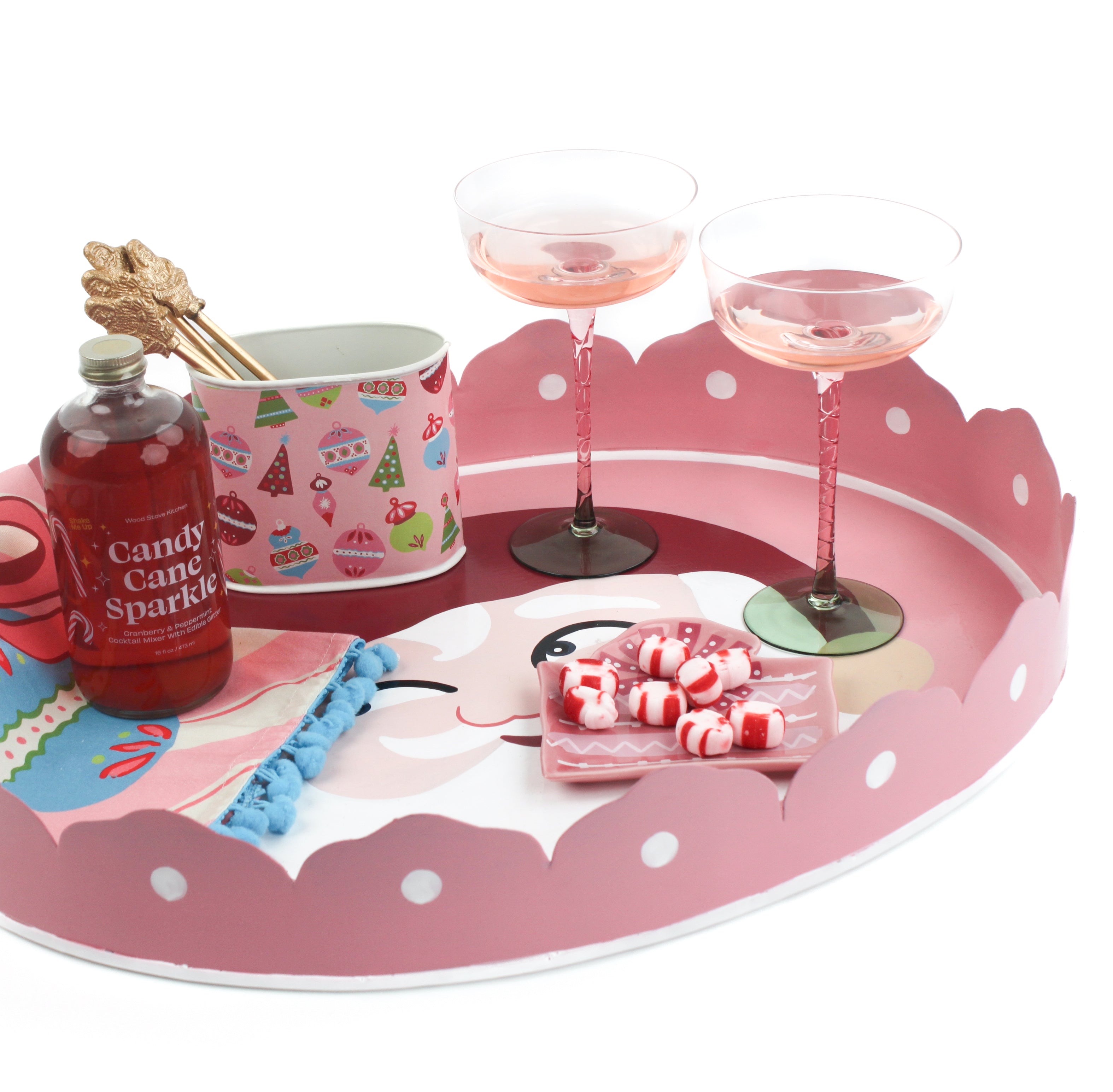 Pink christmas tray with a santa face on the bottom filled with candy and drinks on a white background