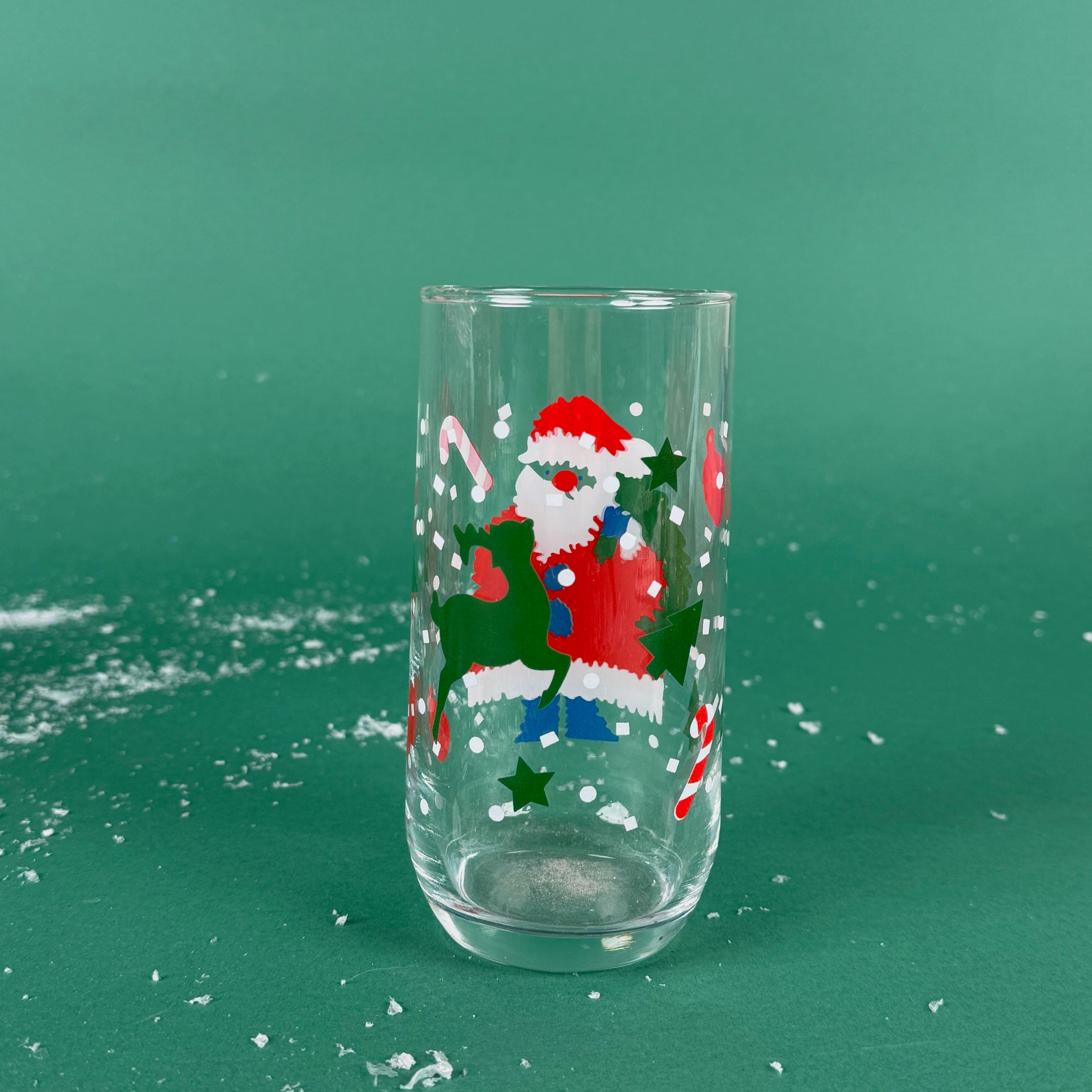 Clear drinking glass with a festive Santa Claus design, candy canes, and stars on a green background with faux snow