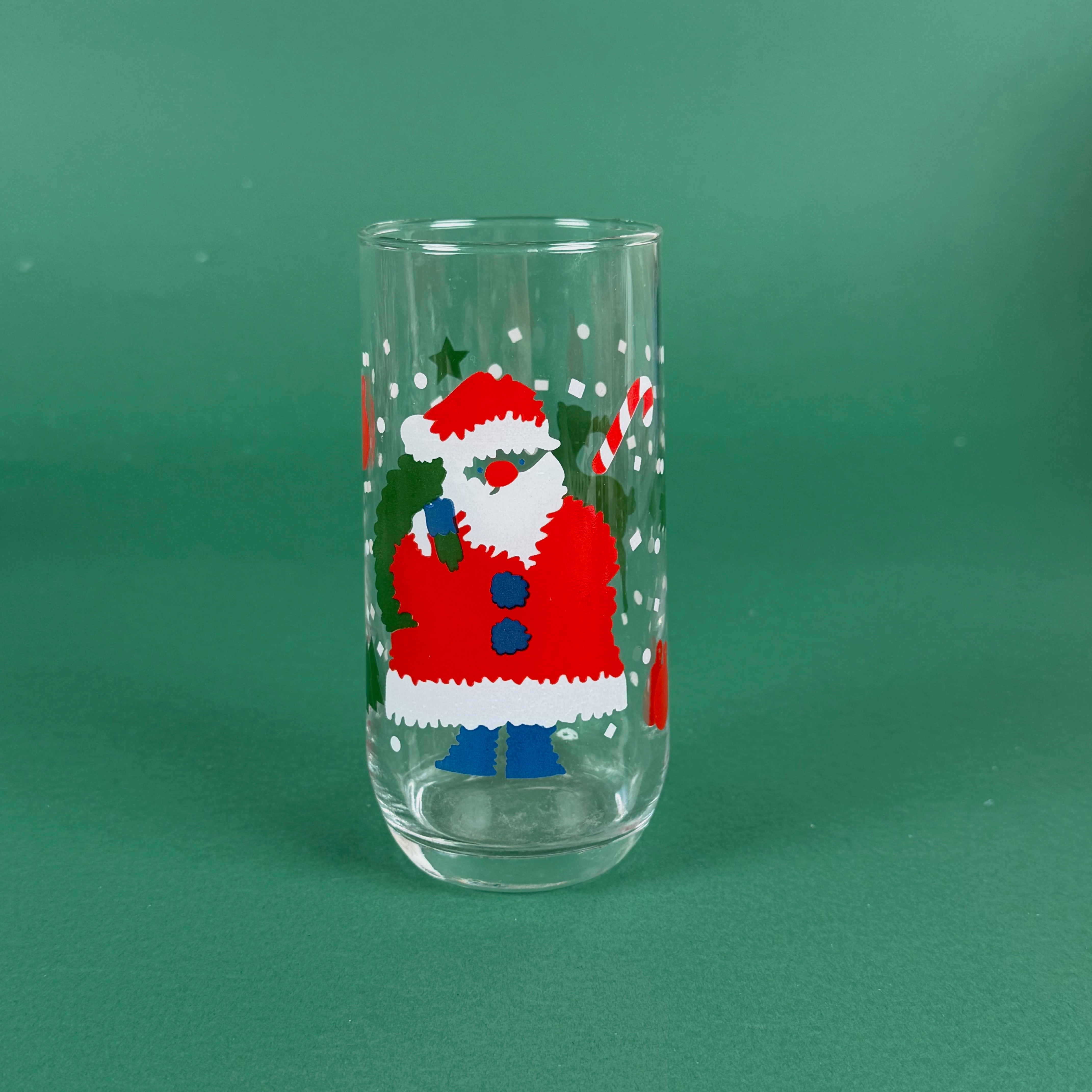 clear drinking glasses with festive Santa Claus designs, holiday on a green background