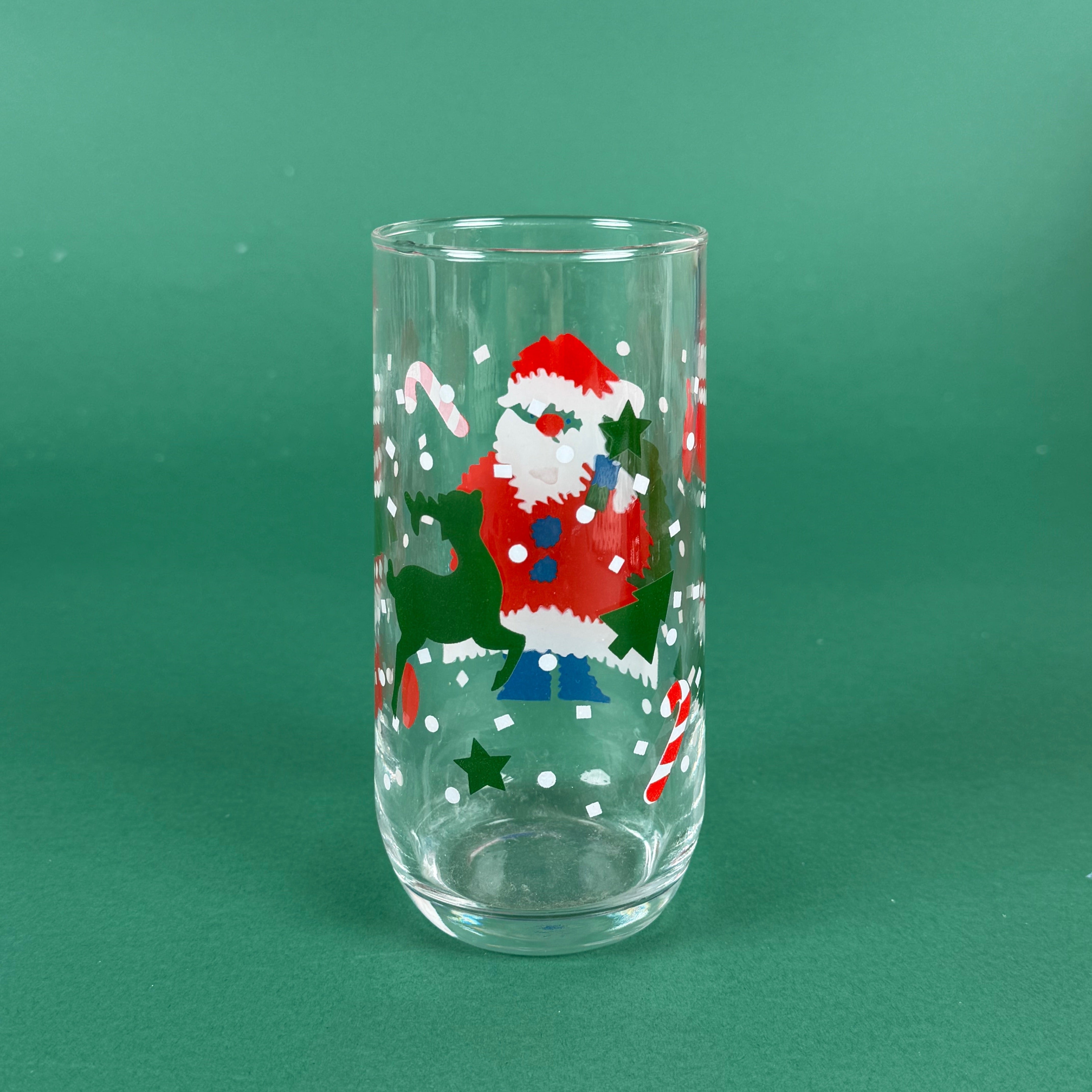 clear drinking glasses with festive Santa Claus designs, holiday on a green background