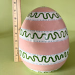 a striped pink large decorative easter egg in tole metal and a ruler in the background to illustrate scale
