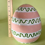 a striped pink large decorative easter egg in tole metal and a ruler in the background to illustrate scale