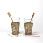 two seagrass wrapped glasses from madcap cottage each with a pineapple swizzle stick inside. 
