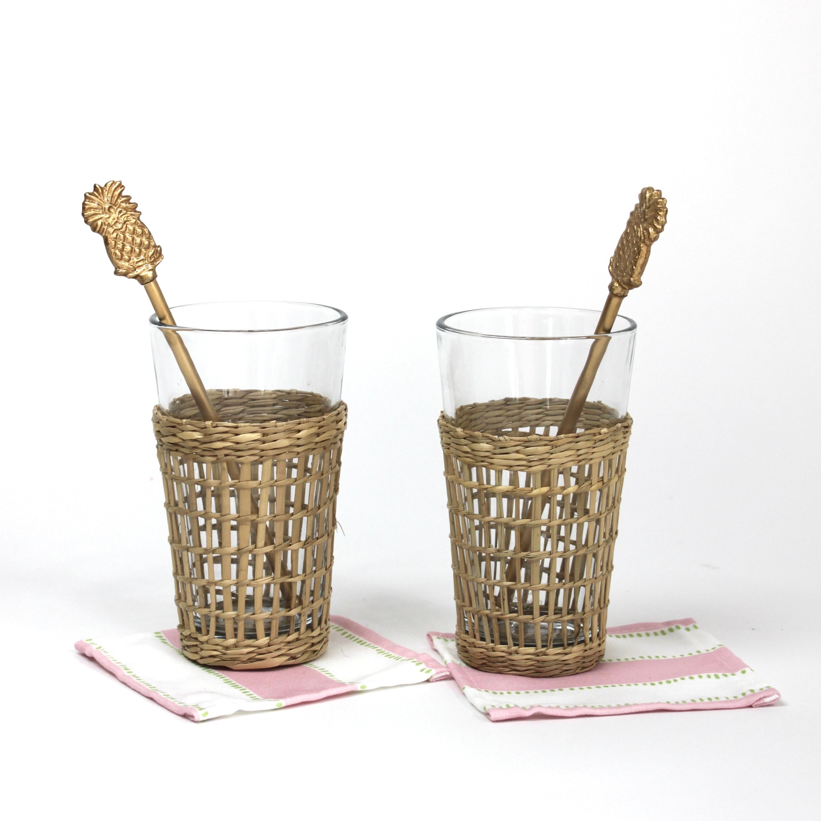 two seagrass wrapped glasses from madcap cottage each with a pineapple swizzle stick inside. 
