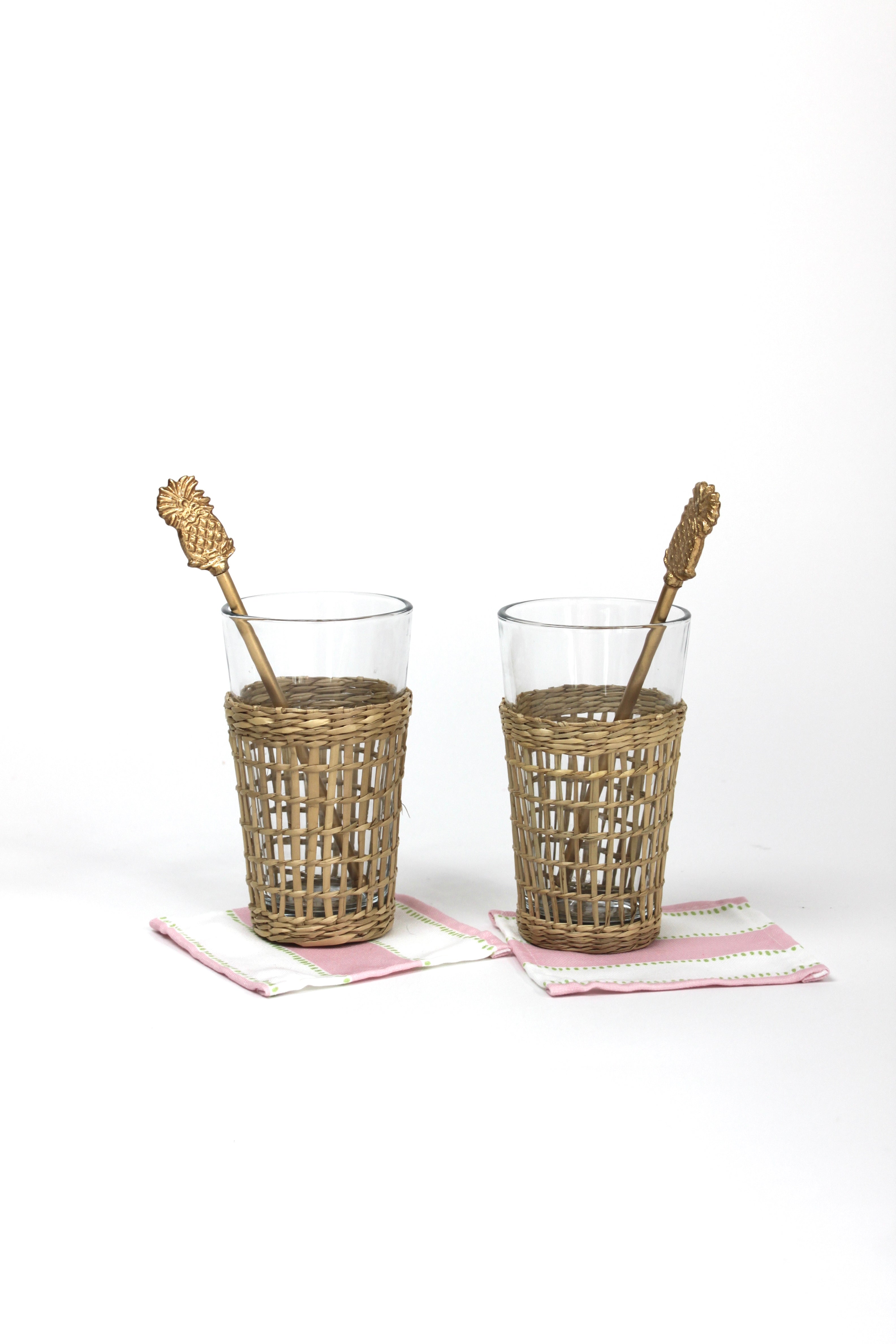 two seagrass wrapped glasses from madcap cottage each with a pineapple swizzle stick inside. 