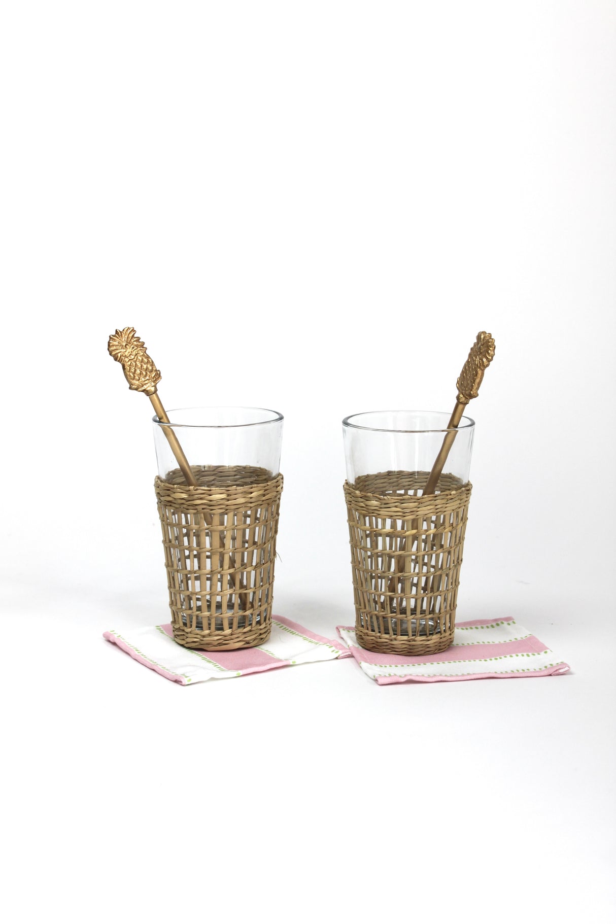 two seagrass wrapped glasses from madcap cottage each with a pineapple swizzle stick inside. 