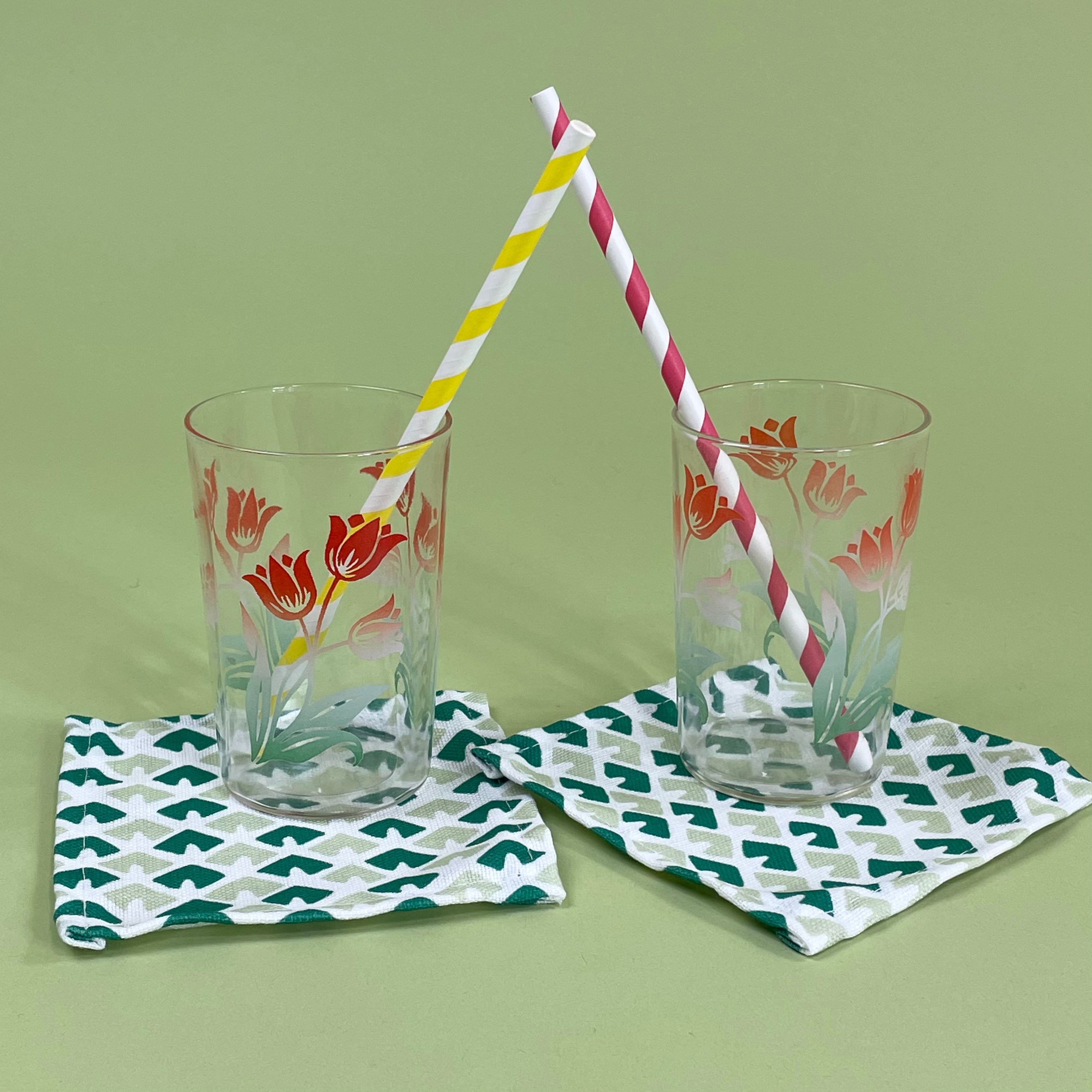 Two glasses with floral tulip design on a green background, each with a striped straw.