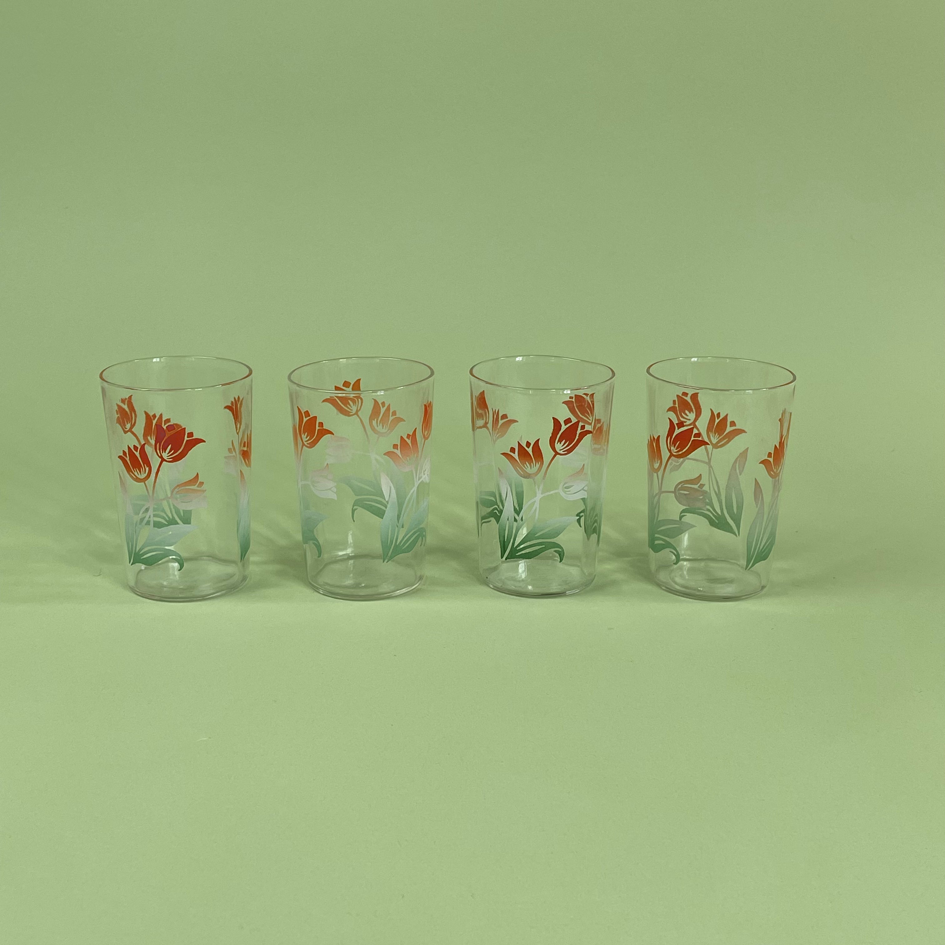 A set of four vintage tulip drinks glasses with floral patterns, displayed against a green background.