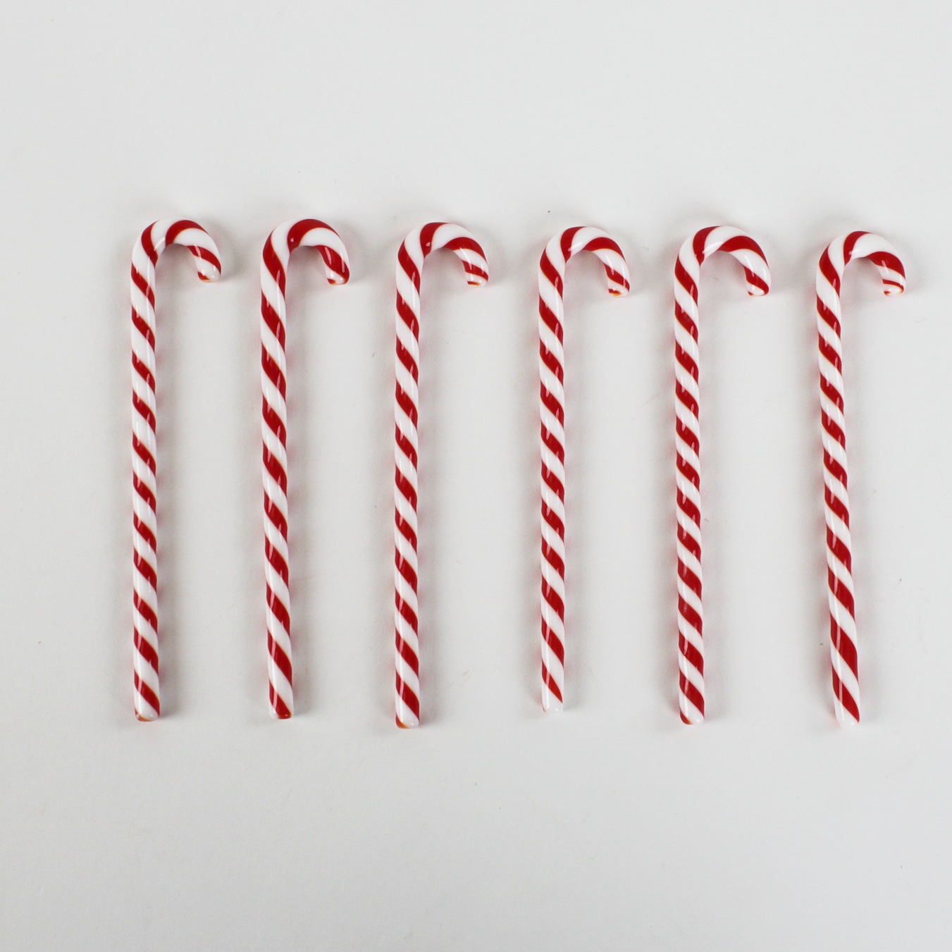 Red and white striped candy canes swizzle sticks on a light gray background