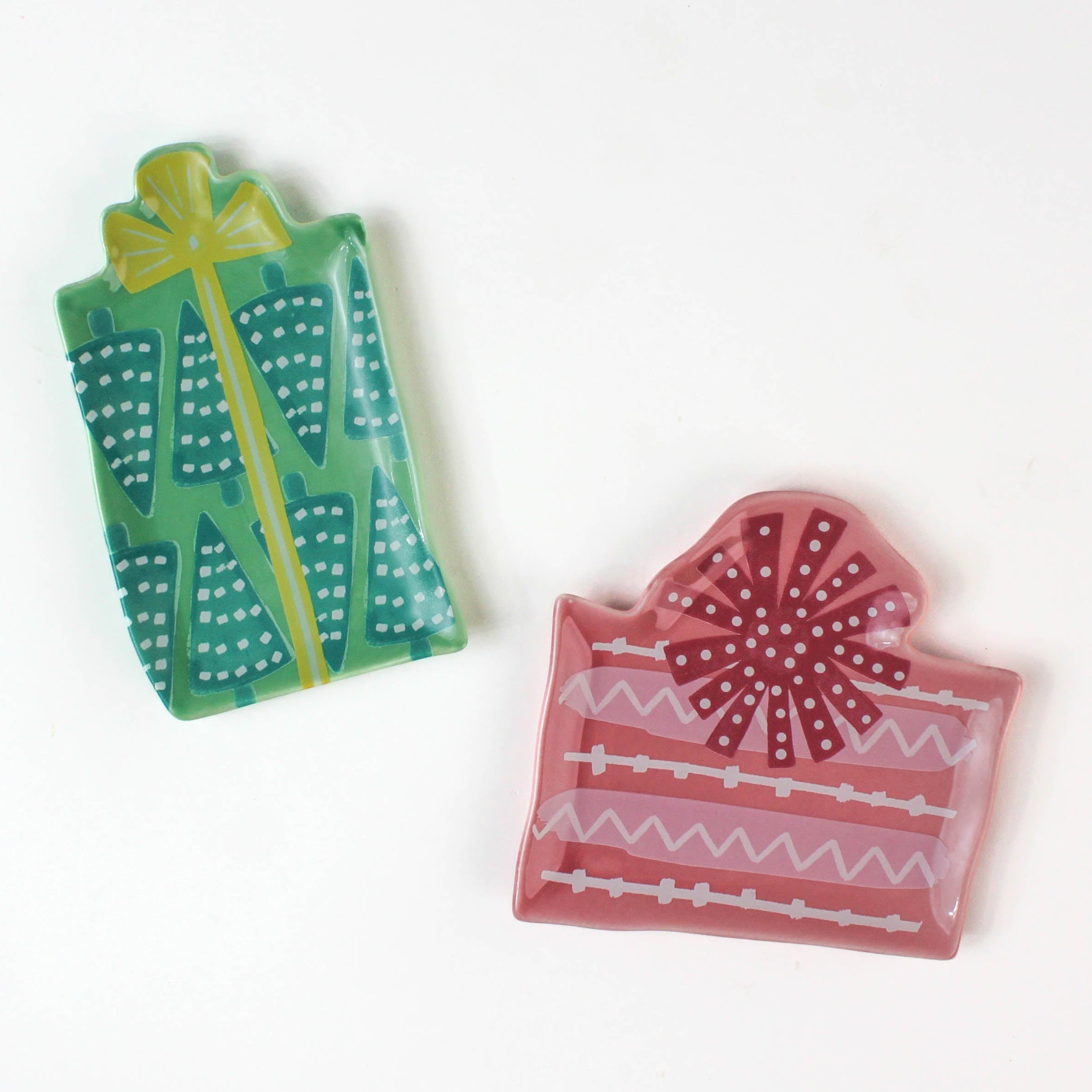set of two christmas accent plates, one plate in the shape of a green gift, the other in the shape of a pink gift, both on a white background.
